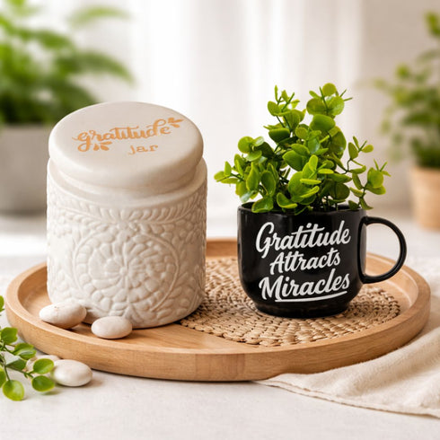 Decorative items including a white jar, black mug with 'Gratitude Attracts Miracles' text, and a small green plant on a wooden tray.