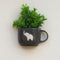 Black mug with white elephant design containing a green plant on a light background